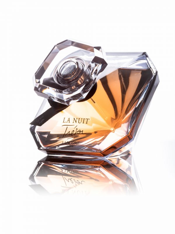 Flacon en verre géométrique et multifacettes du parfum La Nuit Trésor de Lancôme, rempli d'un liquide de couleur ambrée. Le flacon est élégamment conçu avec des bords angulaires, reflétant la lumière sur un fond blanc.